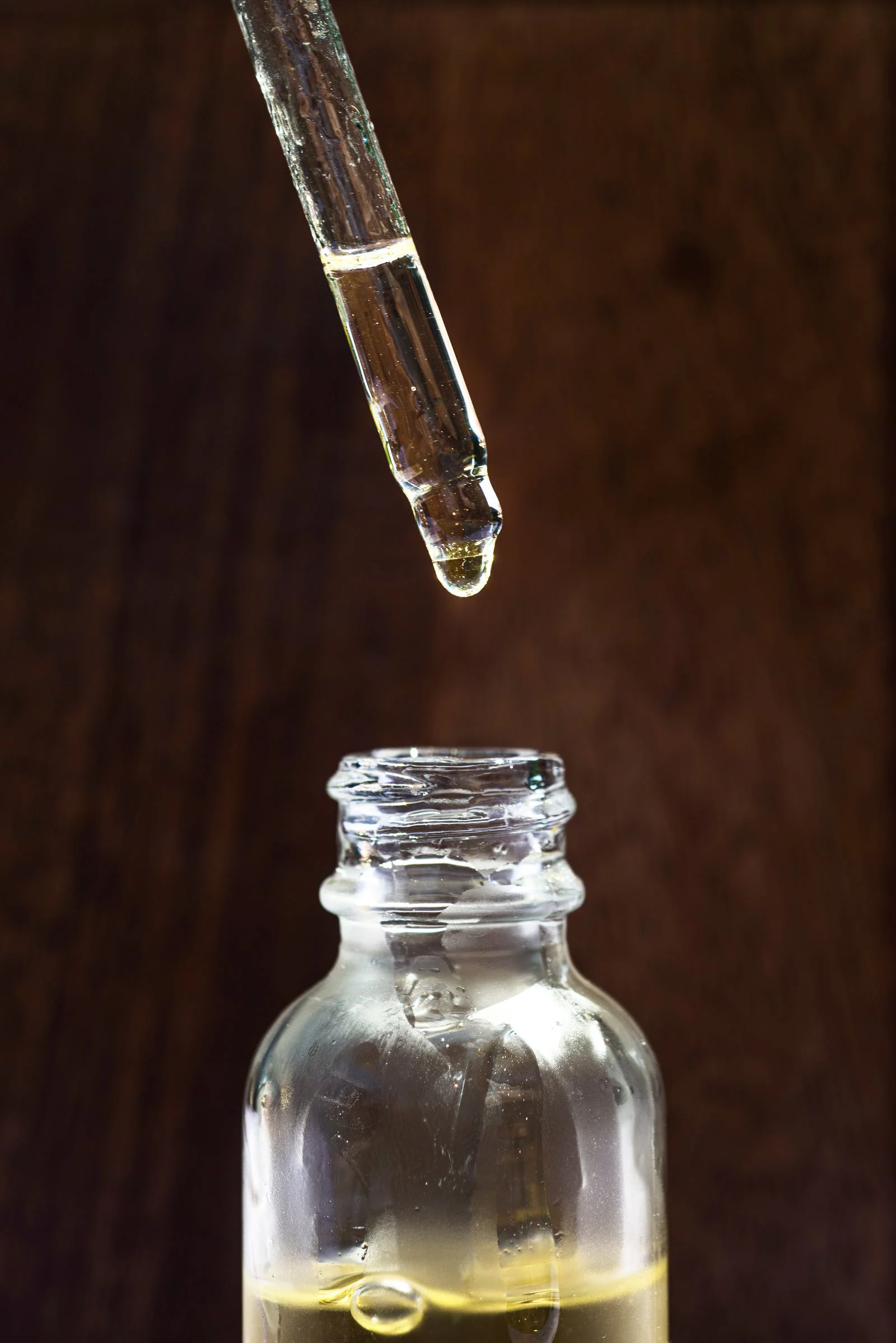 A dropper held above a glass jar of face oil